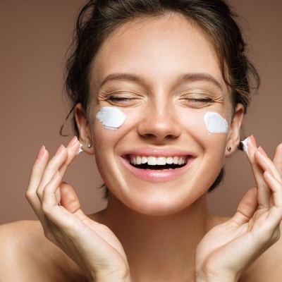 Mulher a aplicar creme facial branco sorridente sobre fundo castanho