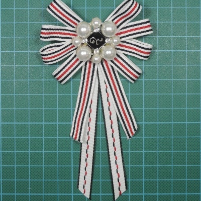 Laço decorativo com fitas às riscas e pérolas ao centro sobre base quadrícula verde