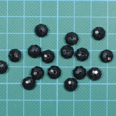 Contas negras facetadas sobre folha de cortar verde com grelha azul