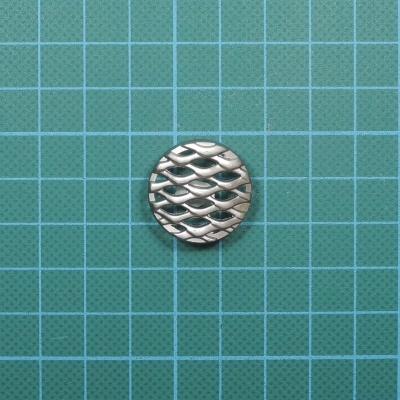 Botão redondo prateado com padrão ondulado sobre fundo verde quadriculado