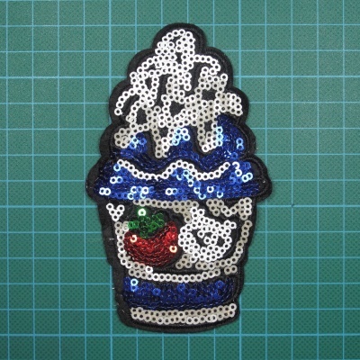 Patch de bebida com chantilly, cereja e detalhes em azul, branco e preto sobre base quadriculada verde