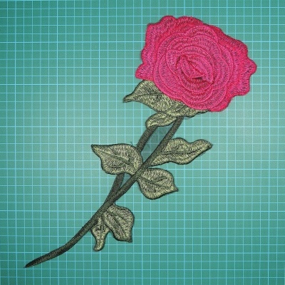 Apliquê bordado de rosa vermelha com folhas verdes sobre régua verde.