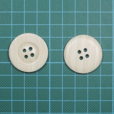 Dois botões redondos de plástico bege claro com quatro furos cada em fundo quadriculado verde