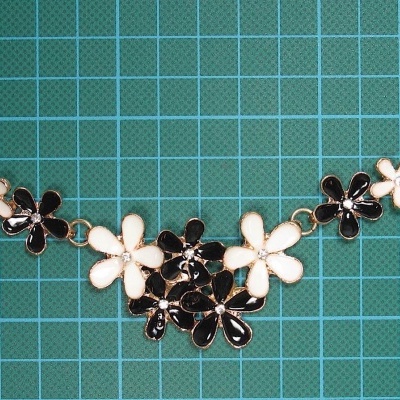 Colar feminino com flores pretas e brancas sobre superfície quadriculada azul