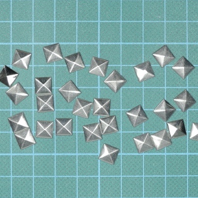 Tachas metálicas quadradas prateadas sobre fundo verde quadriculado