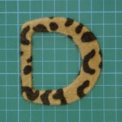 Letra D com padrão peludo tipo leopardo sobre fundo verde quadriculado.