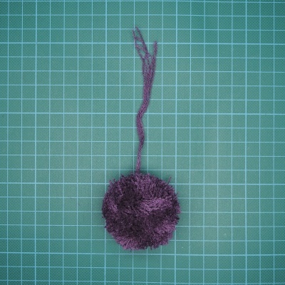 Pom-pom de lã roxo sobre base de corte verde com grelha branca