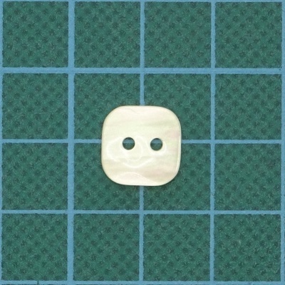 Botão quadrado bege claro com dois orifícios sobre superfície verde com padrão xadrez azul