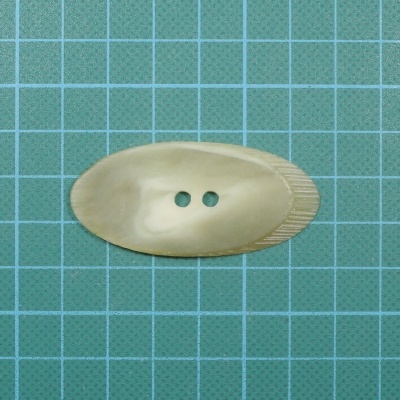 Botão oval bege perolado com duas casas, textura estriada numa extremidade