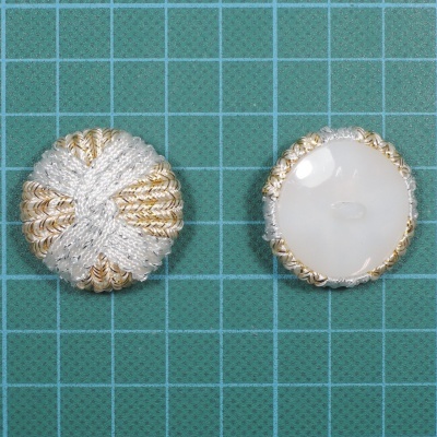 Dois botões redondos com tecido e cordão dourado e prateado sobre superfície verde quadriculada