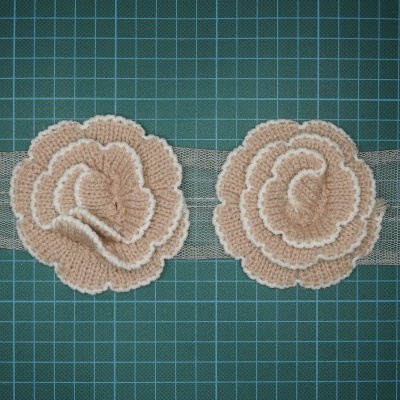 Renda decorativa bege com flores em relevo sobre fundo quadriculado verde.