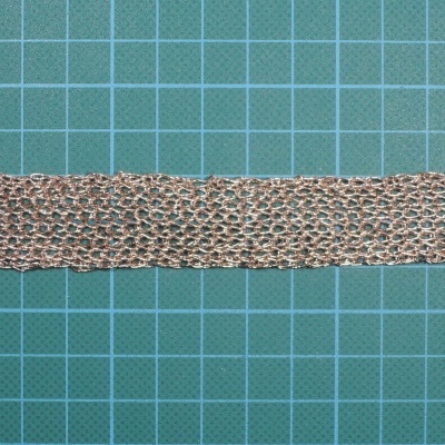 Tira de malha metálica dourada sobre base de corte verde com grelha