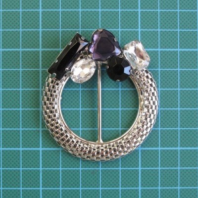 Alfinete de metal prateado com pedras decorativas coloridas