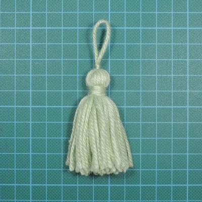 Borla decorativa creme sobre fundo quadriculado verde e branco.