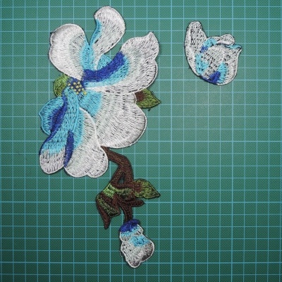 Apliques bordados de flor em branco, azul e verde sobre superfície com padrão de grelha verde