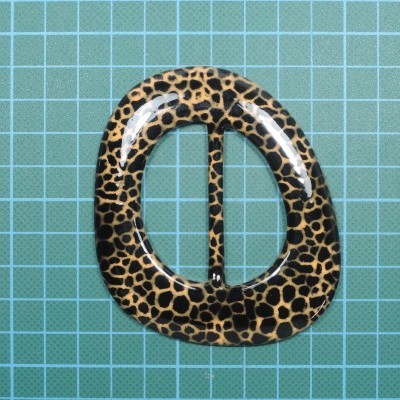 Fivela oval com padrão animal castanho e preto sobre superfície quadriculada azul