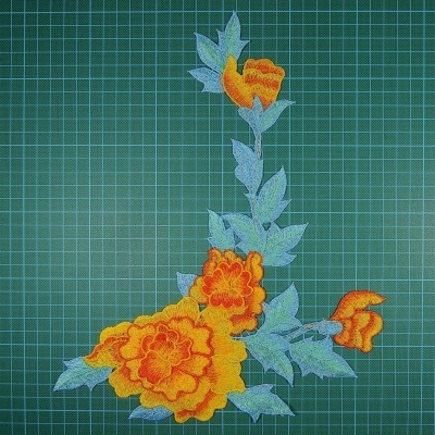 Aplicação de tecido bordado amarelo e laranja com folhas verdes sobre fundo quadriculado verde