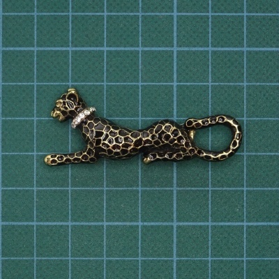 Broche de leopardo dourado e negro com colar branco brilhante sobre superfície verde quadriculada