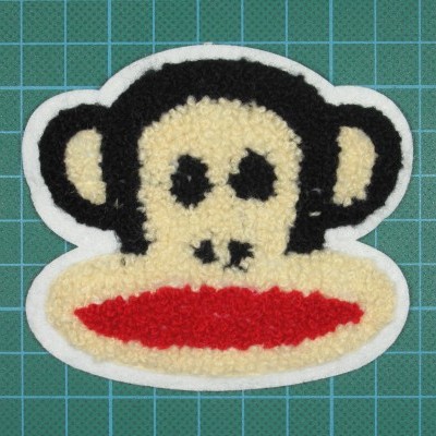 Patch têxtil com rosto de macaco felpudo em cores creme, preto e vermelho