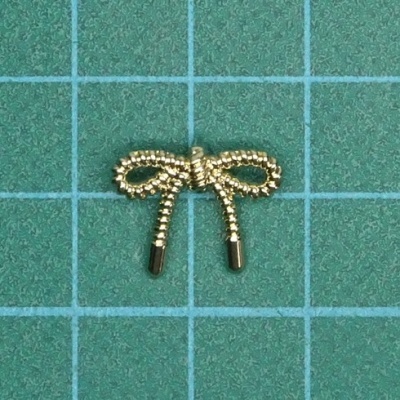 Laço metálico dourado pequeno sobre superfície verde com grelha azul