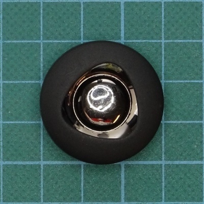 Botão redondo metálico e preto sobre superfície quadriculada verde