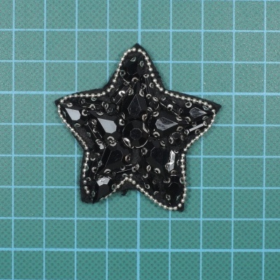 Aplicação em forma de estrela preta com contas e espelhos sobre superfície de corte verde com grade branca.