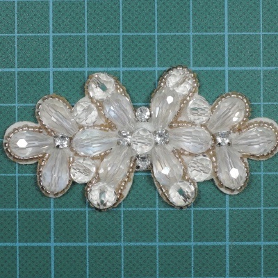 Aplique floral transparente com bordado dourado sobre superfície quadriculada verde