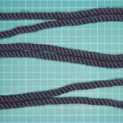 Cordão preto trançado com nós e peças castanhas numa superfície verde quadriculada