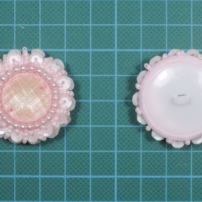 Dois botões redondos rosa claro com rendilhado em fundo verde quadriculado