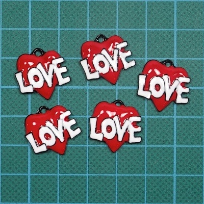 Pendentes em forma de coração vermelho com a palavra LOVE em branco numa superfície azul quadriculada.