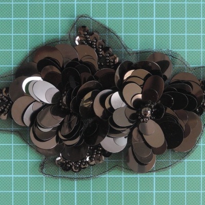 Acessório decorativo em tecido com lantejoulas e contas sobre superfície verde quadriculada