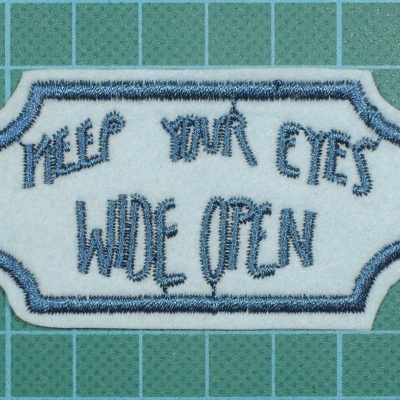 Emblema bordado branco e azul com texto em fundo verde de corte com linhas de grade