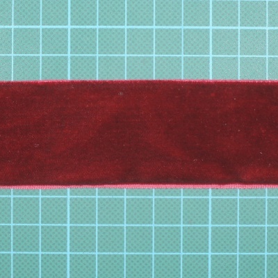 Fita de veludo vermelha com bordas rosas sobre superfície de corte verde-água