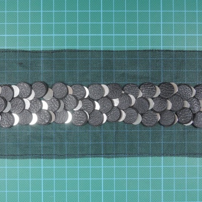 Faixa preta com lantejoulas prateadas em fileiras sobre superfície verde com grelha