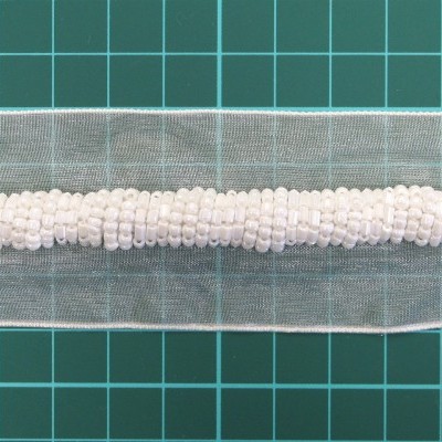 Fita decorativa transparente com contas brancas sobre superfície verde quadriculada