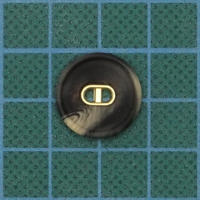 Botão redondo preto e bege sobre superfície verde com padrão xadrez azul