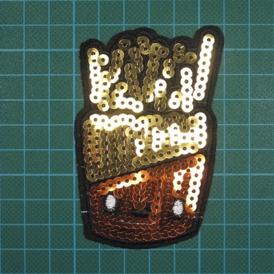 Patch de tecido com desenho de saco de batatas fritas em lantejoulas douradas, castanhas e brancas