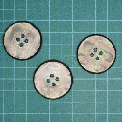 Três botões perolados com quatro furos sobre fundo quadriculado verde