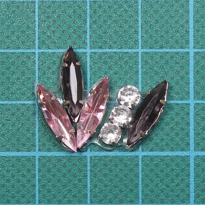 Peças de bijuteria com pedras falsas rosa, roxo e branco sobre superfície verde quadriculada
