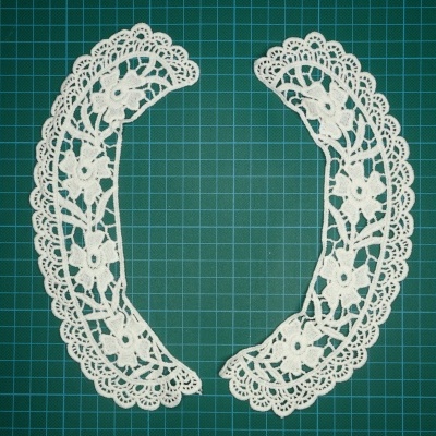 Par de golas de renda branca com padrão floral sobre superfície verde quadriculada