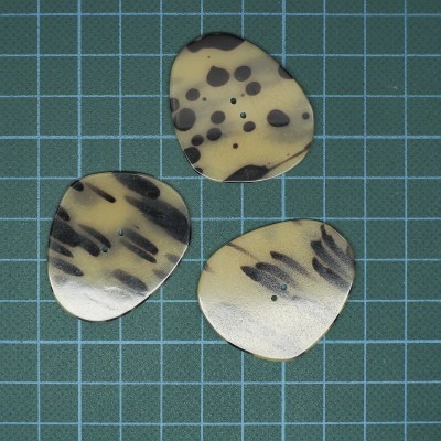 Três palhetas de guitarra bege com manchas pretas sobre fundo quadriculado azul e verde