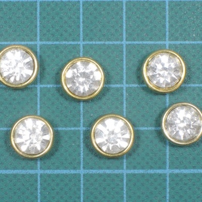 Botões redondos com pedras transparentes e aro dourado sobre superfície verde quadriculada