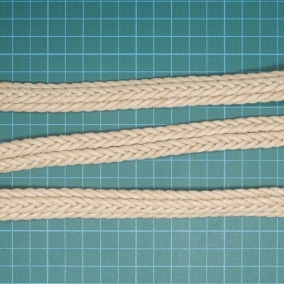 Cinto trançado bege com fivela redonda sobre superfície verde quadriculada