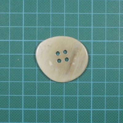 Botão redondo creme com quatro furos sobre fundo verde de grade quadrada