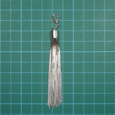 Chaveiro tassel prateado com correntes finas em fundo verde quadriculado