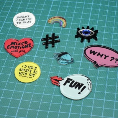 Conjunto de 9 pins esmaltados coloridos com textos e símbolos variados sobre base verde quadriculada