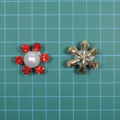 Dois pequenos acessórios decorativos, um com pérola e pedras vermelhas, outro metálico em forma de estrela