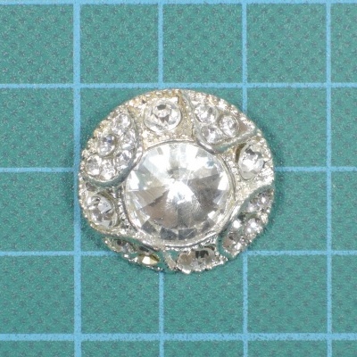 Botão decorativo redondo prateado com pedra central translúcida sobre grelha azul