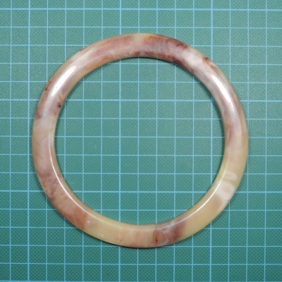 Pulseira circular castanha e bege com padrão marmoreado sobre superfície verde quadriculada