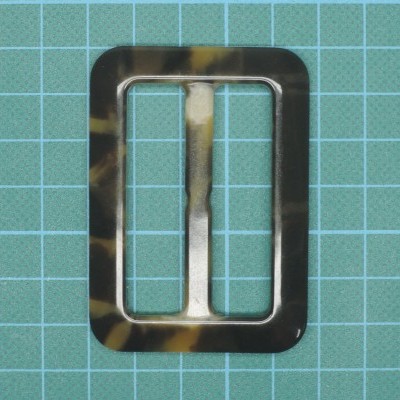 Fivela retangular de plástico marmoreado em tom castanho e preto sobre superfície quadriculada